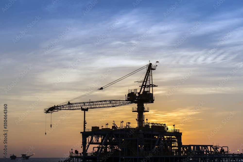 Silhouette of a crane on an oil production platform at oil field during sunset