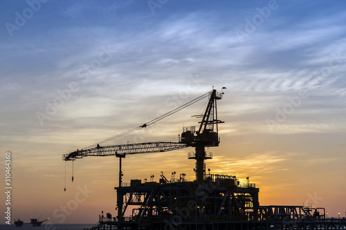 Silhouette of a crane on an oil production platform at oil field during sunset