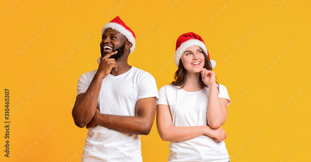 Obraz premium Pensive couple wearing santa hats and posing with thoughtful face expression