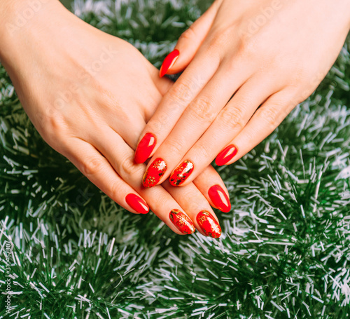 Woman hands with professional red manicure on background of Christmas green tinsel. © Oxana