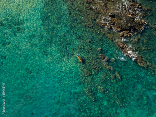 A drone, birds eye view of the bright teal waters off the coast of Maui with coral reefs and lava rock coastlines