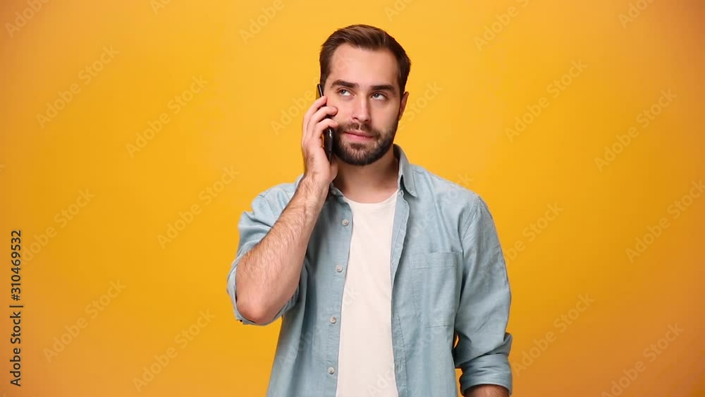 Young guy 20s in denim shirt white t-shirt isolated on yellow background in studio. People lifestyle concept. Looking on mobile phone. Doesn't want talk on cellphone, showing gesture bla-bla with hand Young guy 20s in denim shirt white t-shirt isolated on yellow background in studio. People lifestyle concept. Looking on mobile phone. Doesn't want talk on cellphone, showing gesture bla-bla with hand