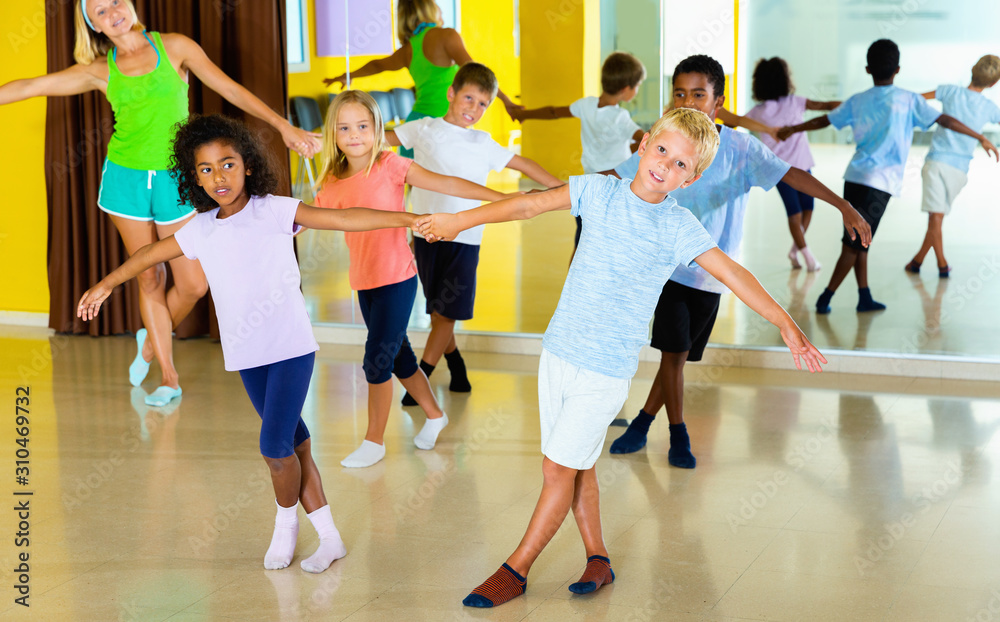 Group of children practicing vigorous jive movements in dance class with female coach