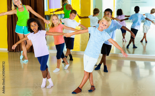 Group of children practicing vigorous jive movements in dance class with female coach