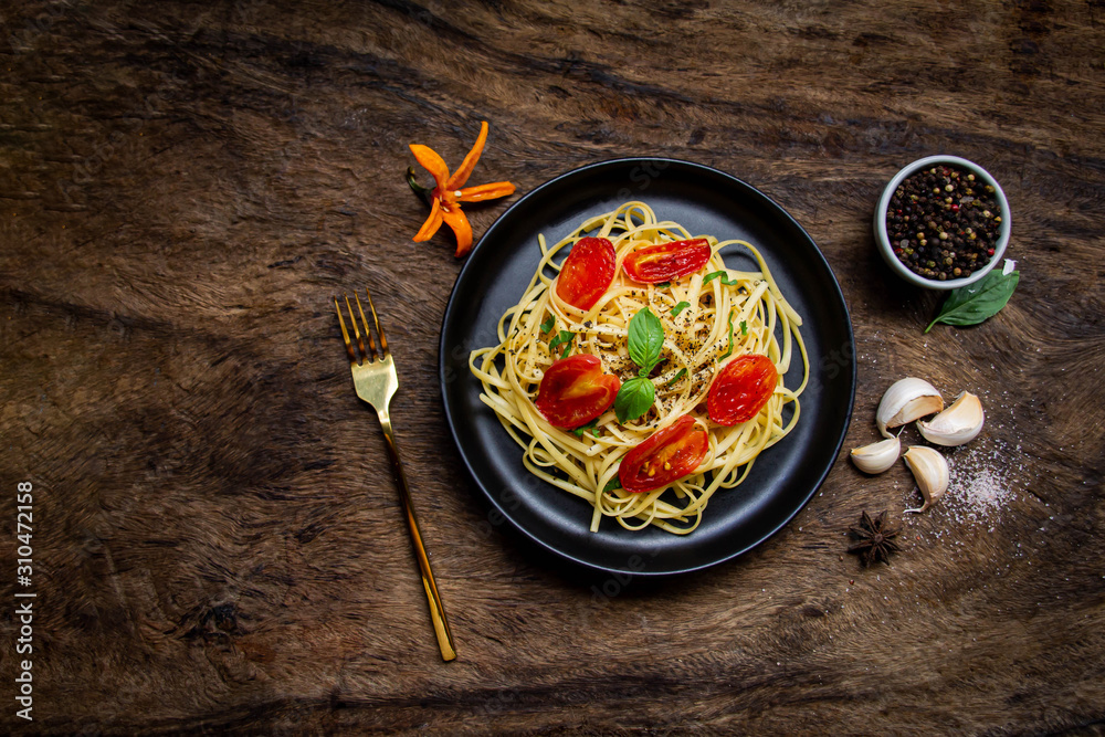 Italian spaghetti pasta with tomatoes and basil on a plate on a dark table and garlic A cup of pepper placed beside View from above, horizontal