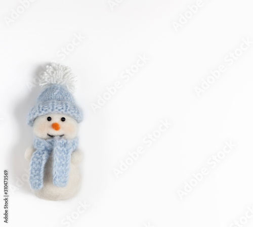 Cute funny snowman in blue hat and scarf on white background. Christmas wool toy.