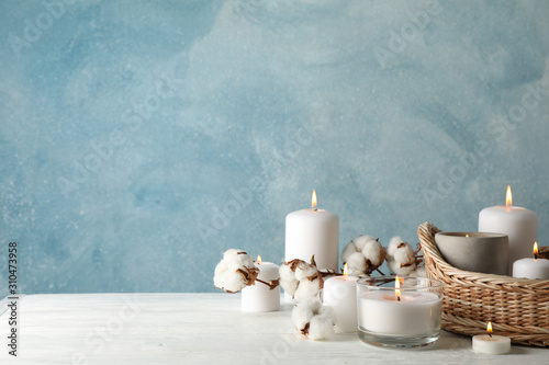 Burning candles, basket and cotton on white wooden table, space for text photo