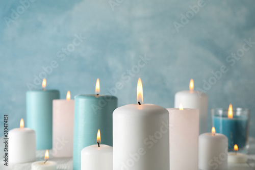 Different burning candles against blue background, space for text