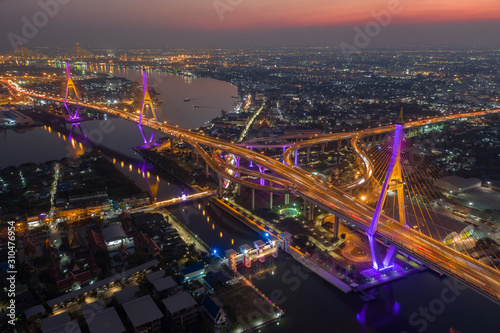 Evening bridge with lights on the bridge over the Chao Phraya River. Aerial view of the Bhumibol Adulyadej Suspension Bridge over the Chao Phraya River in Bangkok with cars on the bridge at the sunset