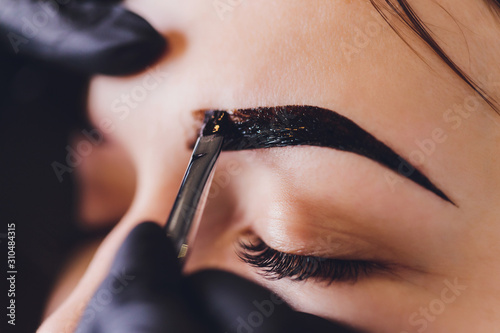 beautician- makeup artist applies paint henna on previously plucked, design, trimmed eyebrows in a beauty salon in the session correction. Professional care for face. photo