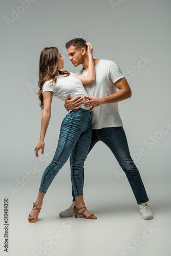 dancers in t-shirts and jeans dancing bachata on grey background