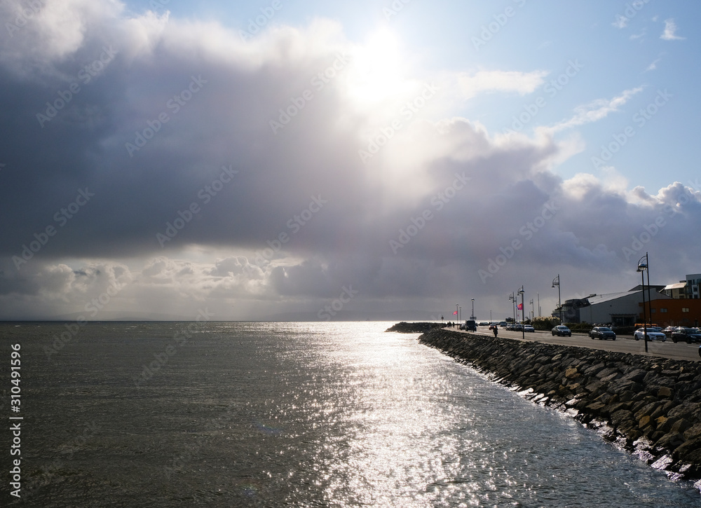 View of Salthill promenade and Galway Bay in Ireland at sunset, with sunlight reflecting on the water and clouds in the sky.