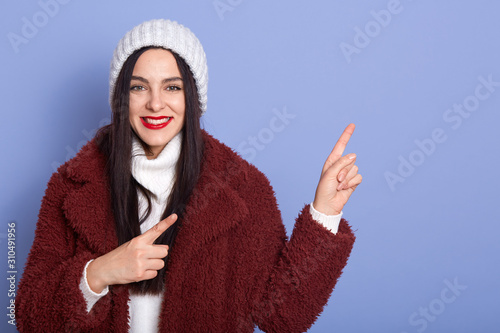 Horizontal studio shot of good looking pretty model making gestures, pointing with forefingers, looking directly at camera, standing isolated over lilac background. Copyspace for advertisement. photo