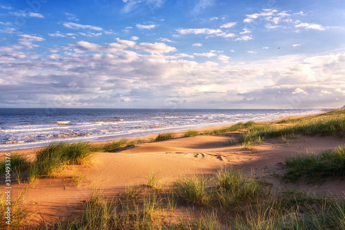 Amazing seascape in soft sunset light with sand dunes, green grass, waves of the sea and blue sky with clouds. Outdoor travel background, Northern sea, Netherlands
