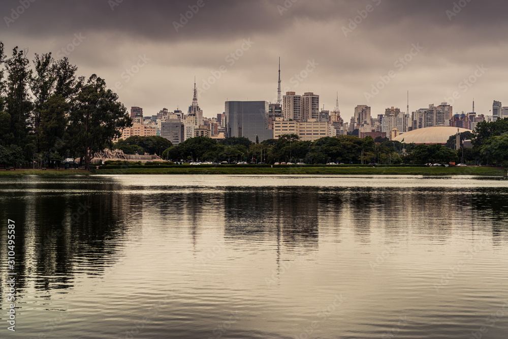 Fototapeta premium Cidade de São Paulo em tarde chuvosa, com reflexo em lago no Parque do Ibirapuera, São Paulo, Brasil