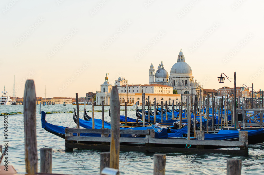 Gold sunset with gondolas docked in Grand Canal, Venice, Italy. Bright sunny panorama view of Grand Canal with gondola and church. Beautiful photo background of the venetian canal in the morning.