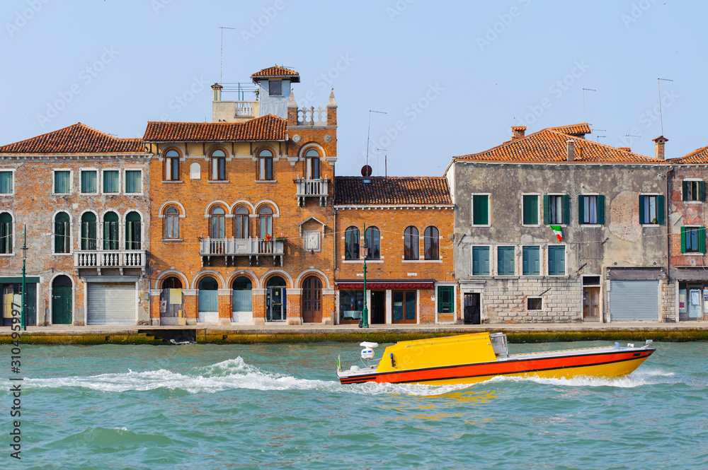 Yellow boat in Grand Canal, Venice, Italy. Bright sunny panorama view of Grand Canal with old brick buildings. Beautiful photo background of the venetian canal.
