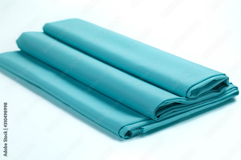The scouring of cotton fabric with satin effect of blue color is beautifully laid in a roll on a white isolated background The scouring of cotton fabric with satin effect of blue color is beautifully laid in a roll on a white isolated background