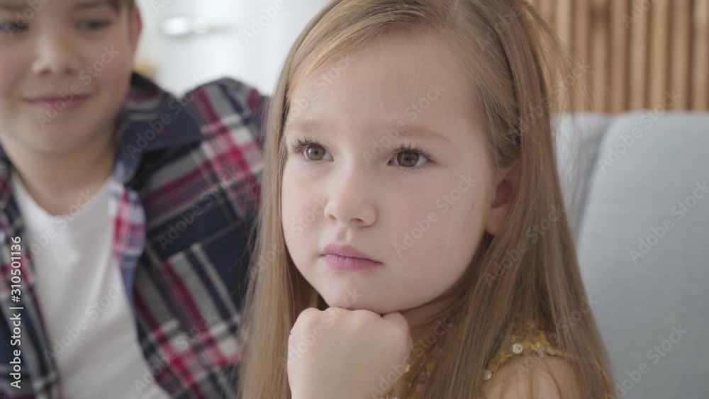 Close-up portrait of sad Caucasian girl with brown eyes looking at camera and away as blurred boy caressing her head at the background. Friend calming down upset lady. Friendship, first love, care. Close-up portrait of sad Caucasian girl with brown eyes looking at camera and away as blurred boy caressing her head at the background. Friend calming down upset lady. Friendship, first love, care.