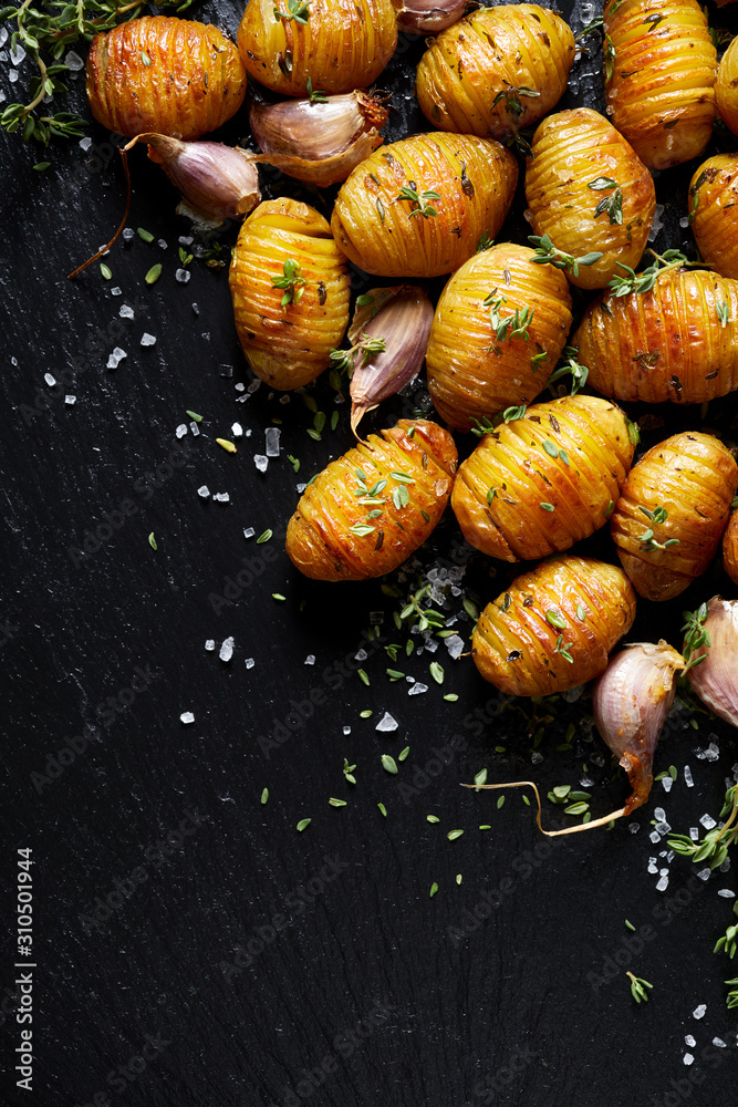 Baked potatoes hasselback with garlic and thyme on a black background with copy space, to