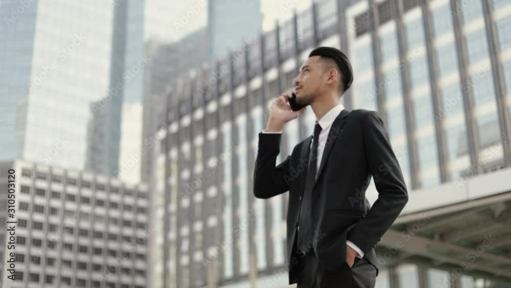 Portrait handsome businessman in a black suit talking on the phone while standing outside on the street near a big office building urban. Portrait handsome businessman in a black suit talking on the phone while standing outside on the street near a big office building urban.