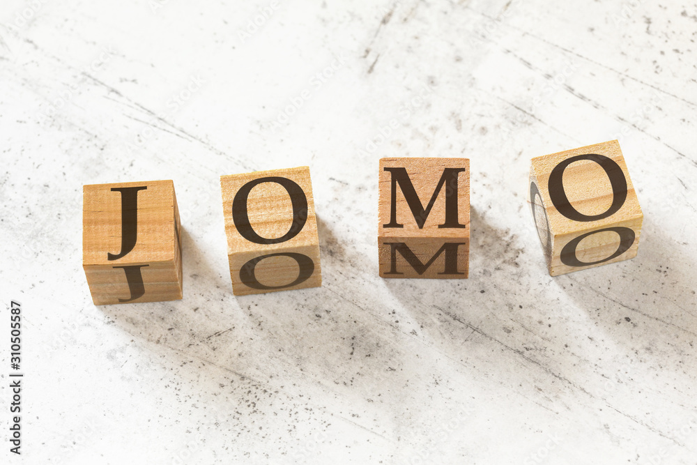 Four wooden cubes with letters JOMO (meaning Joy of missing out) on white working board. Four wooden cubes with letters JOMO (meaning Joy of missing out) on white working board.