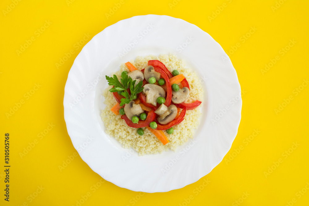 Couscous with vegetables in the white plate in the center of the yellow background. Top view. Copy space. Closeup. Couscous with vegetables in the white plate in the center of the yellow background. Top view. Copy space. Closeup.