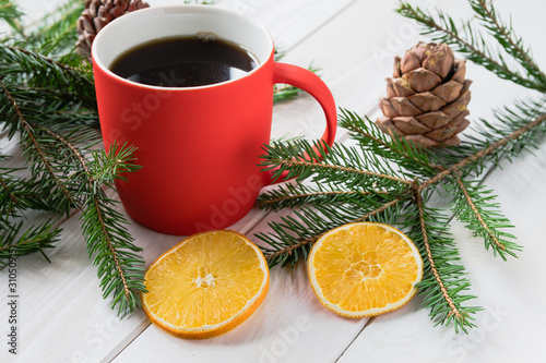 Red cup with a hot drink next to spruce branches and dried lemon slices