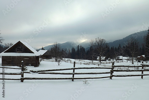 Mountain winter landscape with outbuildings and a fence.
