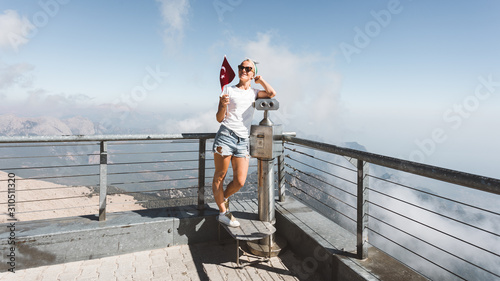 Fototapeta Naklejka Na Ścianę i Meble -  Young woman tourist stands on a viewing platform of Tahtali Mountain in Kemer with a red Turkey flag, Turkey
