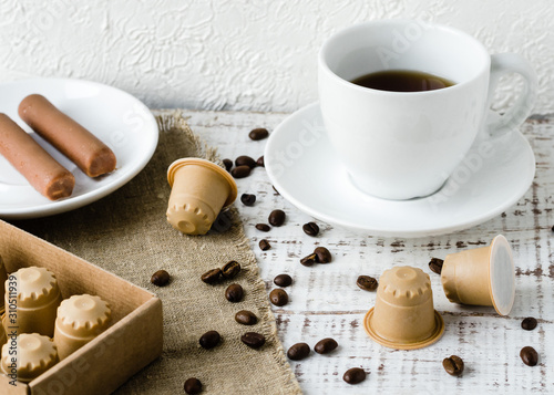 The white cup with wooden coffee capsules and coffee beans on white wooden background. Coffee capsule made of wood. Zero waste and no plastic concept. Eco coffee capsules