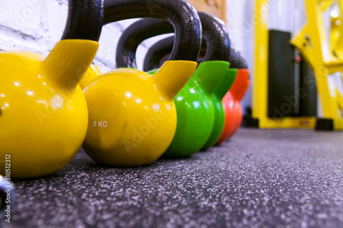 Colorful yellow green and red kettlebells in a row black gym floor background copy space on the front kettle bell. Selective focus. Horizontal image