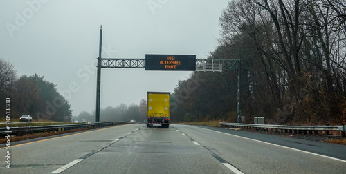 Canvas Print Electric warning sign over yellow box truck on highway advising drivers to use a