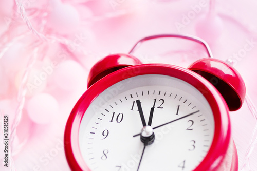 Red vintage alarm clock indicating the time 23:55  closeup and Christmas garlands on a white background. New Year background 