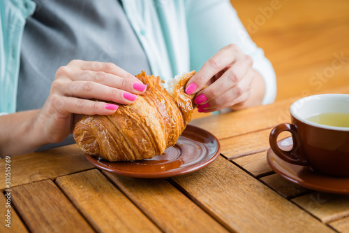 Fényképezés Woman with pink manicure is tearing a small piece from large croissant , aliened