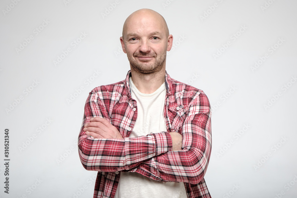 Confident, bald, unshaven man stands with his arms crossed and stares intently at the camera. Confident, bald, unshaven man stands with his arms crossed and stares intently at the camera.