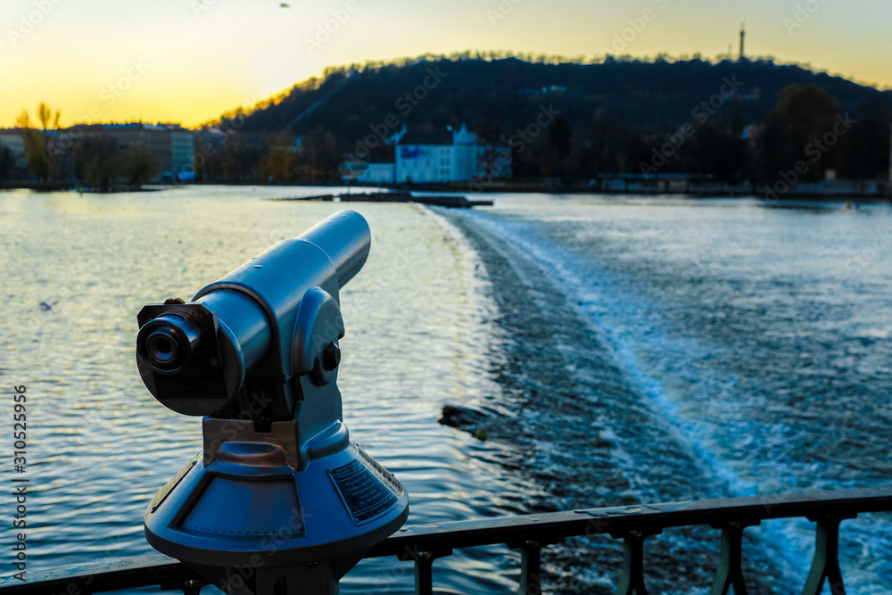 Image of a public telescope on the railing of a bridge in Prague at sunset