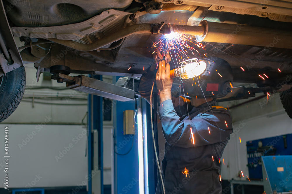 Car mechanic welder welds a damaged part on a car