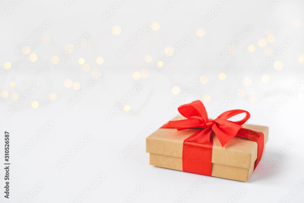 Gift box with a red bow on a background of blurred lights garland. Christmas background.