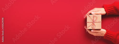 Female's hands in red pullover holding gift box on red background. Christmas and Valentine's Day concept. Banner for website © Olga Zarytska