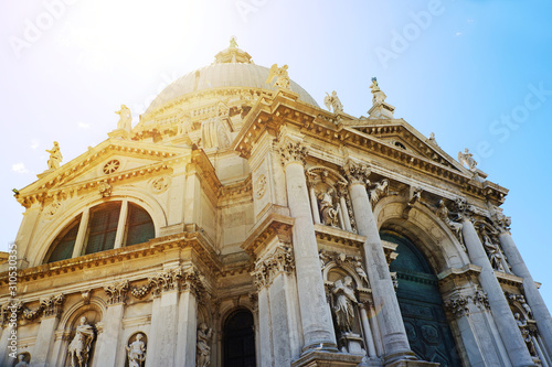 Beautiful view of famous Basilica di Santa Maria della Salute in warm sunset light with sunbeams in Venice, Italy. Cathedral on Grand Canal, old Italian architecture in sunlight with sun rays.