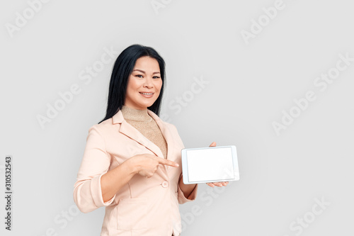 Freestyle. Asian businesswoman standing isolated on white pointing at screen of digital tablet smiling confident copy space