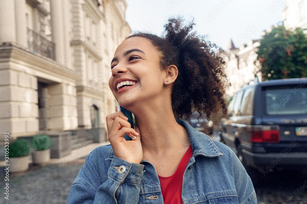 Outdoors Leisure. Young stylish african girl in denim jacket standing talking on phone laughing cheerful close-up