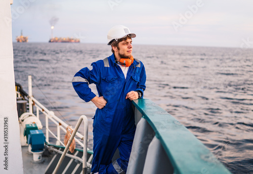 Marine Deck Officer or Chief mate seaman on deck of offshore vessel or ship , wearing PPE personal protective equipment - helmet, coverall looks at sea. ocean view