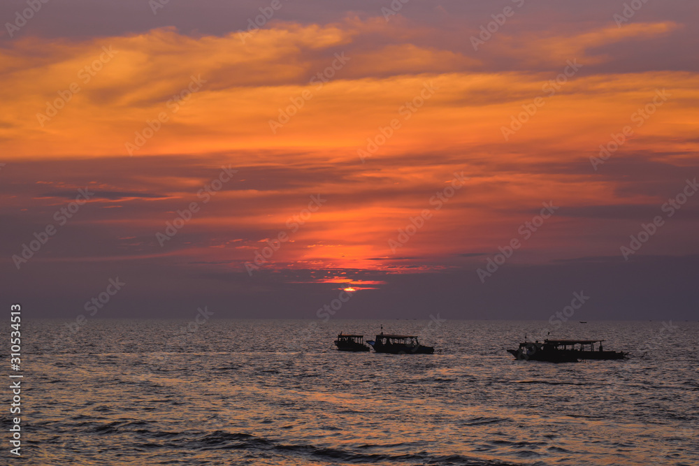 Fisherman boats floating on wide ocean during beautiful orange sunset