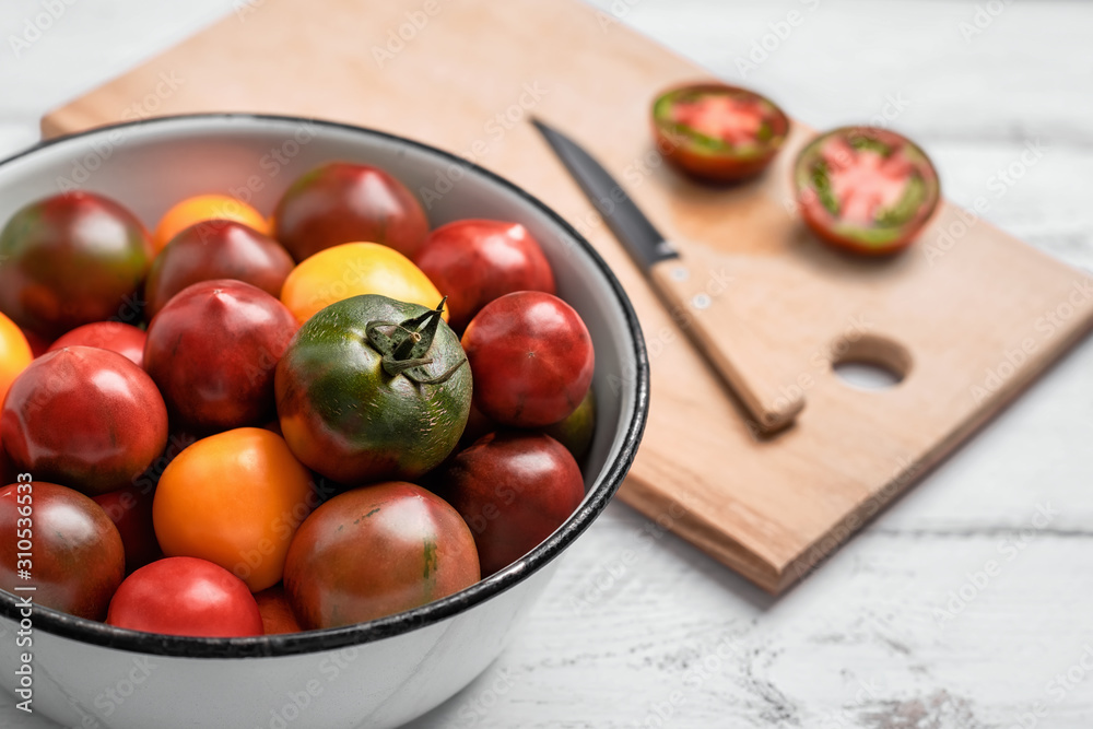 Black prince tomatoes and yellow tomatoes in big enamel bowl, knife and cut tomato on cutting board on white wooden table. Close-up, blurry background Black prince tomatoes and yellow tomatoes in big enamel bowl, knife and cut tomato on cutting board on white wooden table. Close-up, blurry background