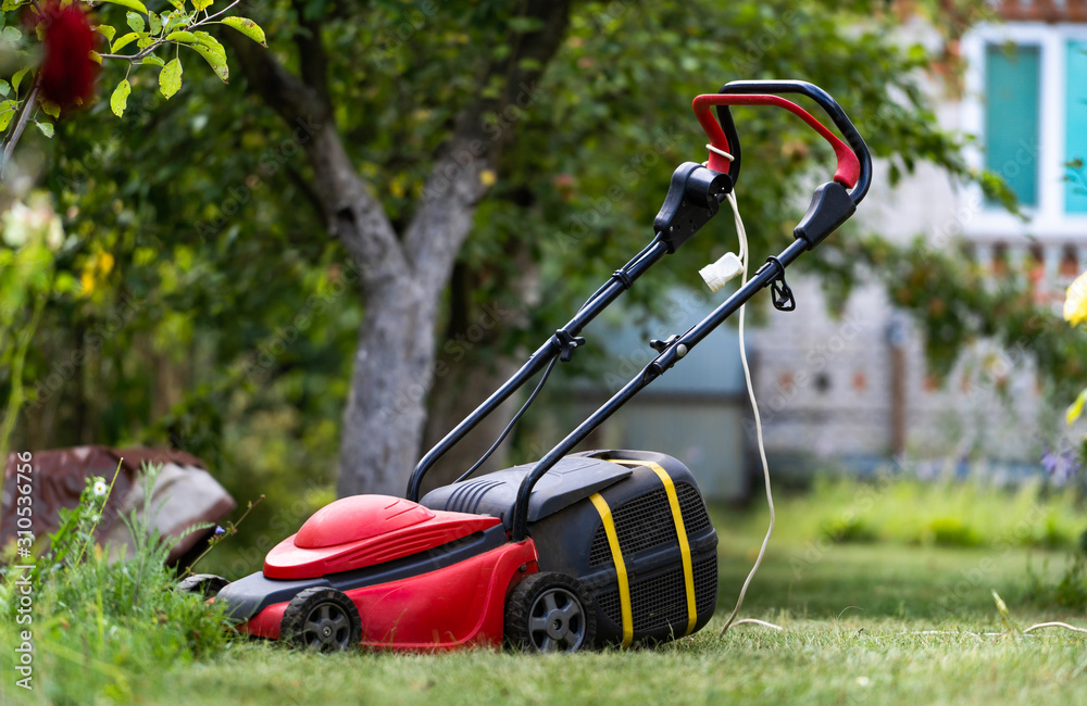 Lawn mower on a lawn in the garden, gardening. Red machine with tank for grass. Gardening concept. Lawn mower on a lawn in the garden, gardening. Red machine with tank for grass. Gardening concept.