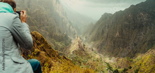 Rear view of traveler making photo of amazing steep mountainous terrain with lush canyon valley on the path from Xo-Xo Valley. Santo Antao Island, Cape Verde photo