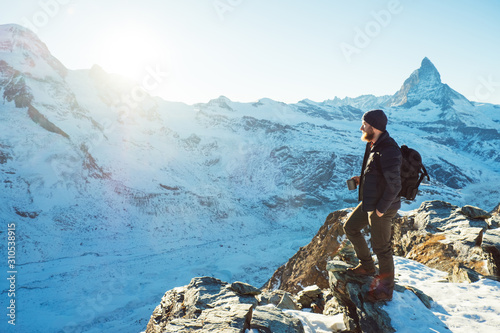 Traveler Man with backpack trekking in mountains, enjoy beautiful Matterhorn view. Explorer man hiking on hills, travel in Swiss Alps, Switzerland. Hiker standing on rock cliff outdoors on nature.