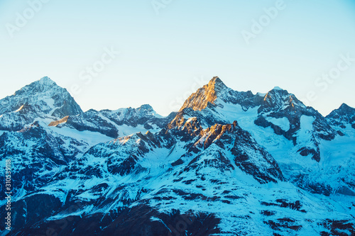 Beautiful nature landscape of Swiss Alps in sunlight rays. Sunset mountains covered with snow in Switzerland. Great view of the snowy rocks and sun beams in Alpine ski resort. Winter holidays.